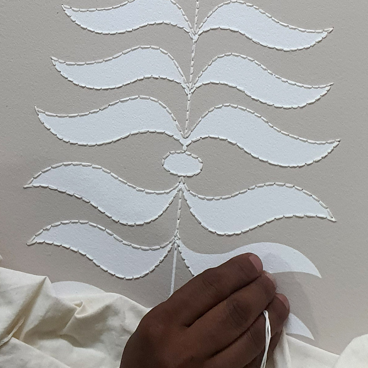 Artisan embroidering fern motif on printed wallpaper using kantha stitch technique.